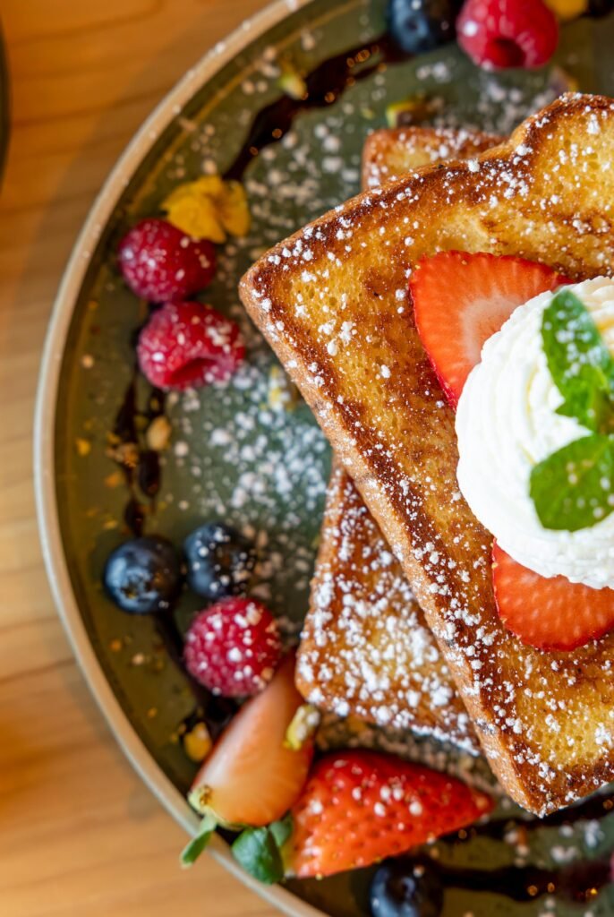 Tasty French toast served with strawberries, blueberries, and raspberries, topped with cream.
